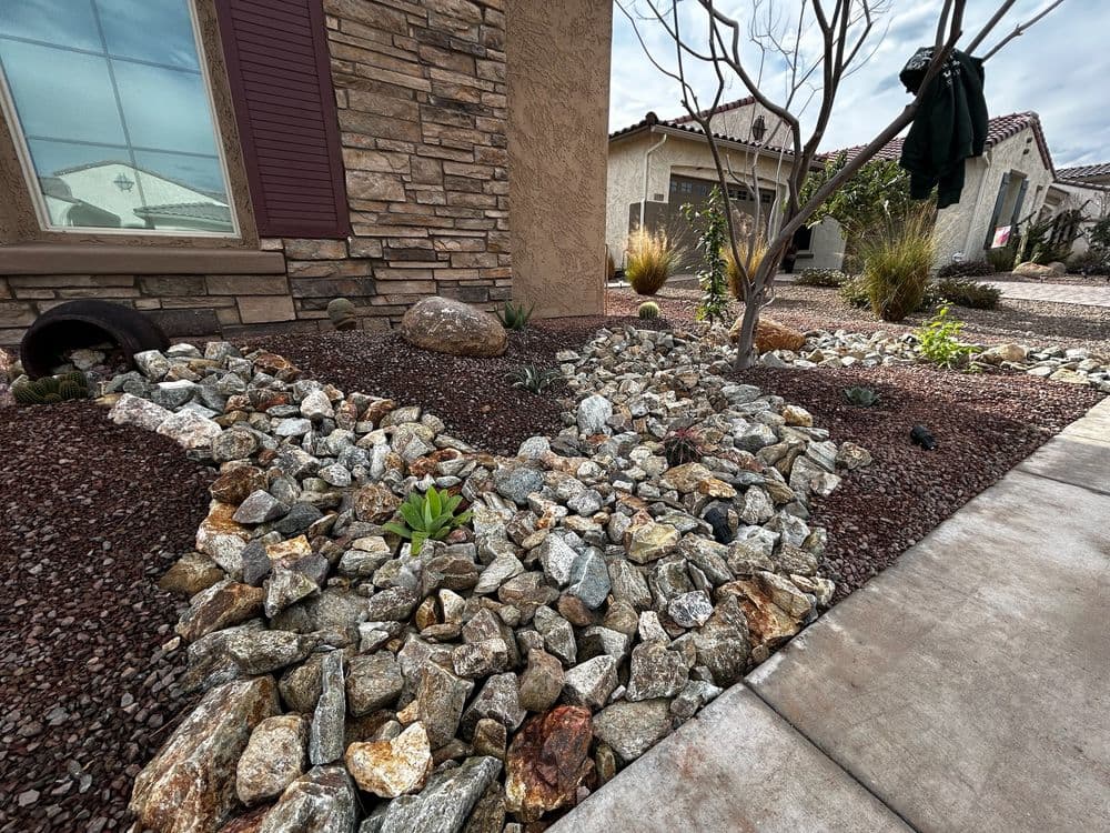 Desert landscape with decorative rocks, plants, and modern home exterior.