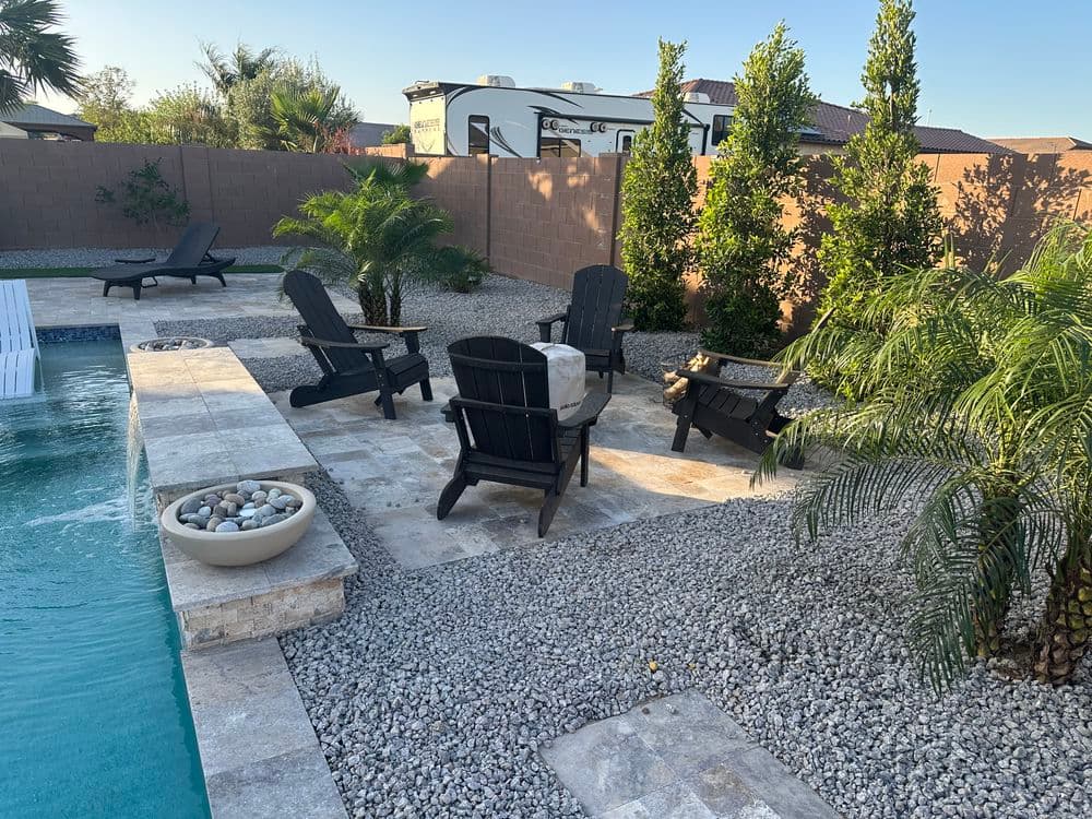 Outdoor pool area with black lounge chairs, fire pit, and lush greenery in a sunny setting.