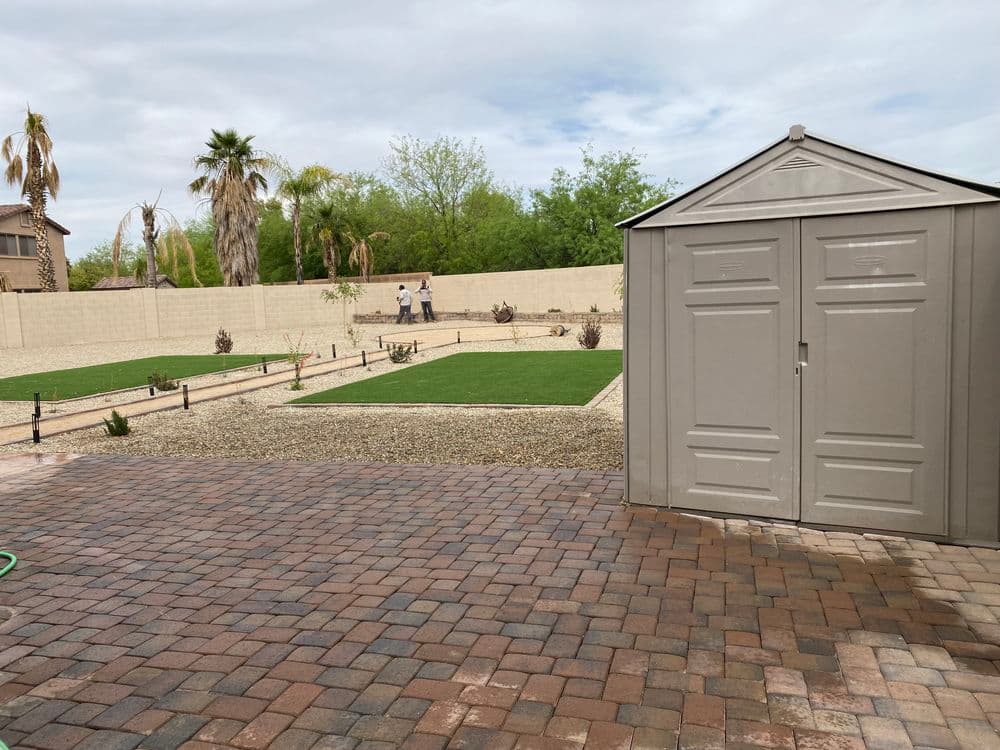 Backyard landscape with a storage shed, gravel areas, and green lawn under a cloudy sky.