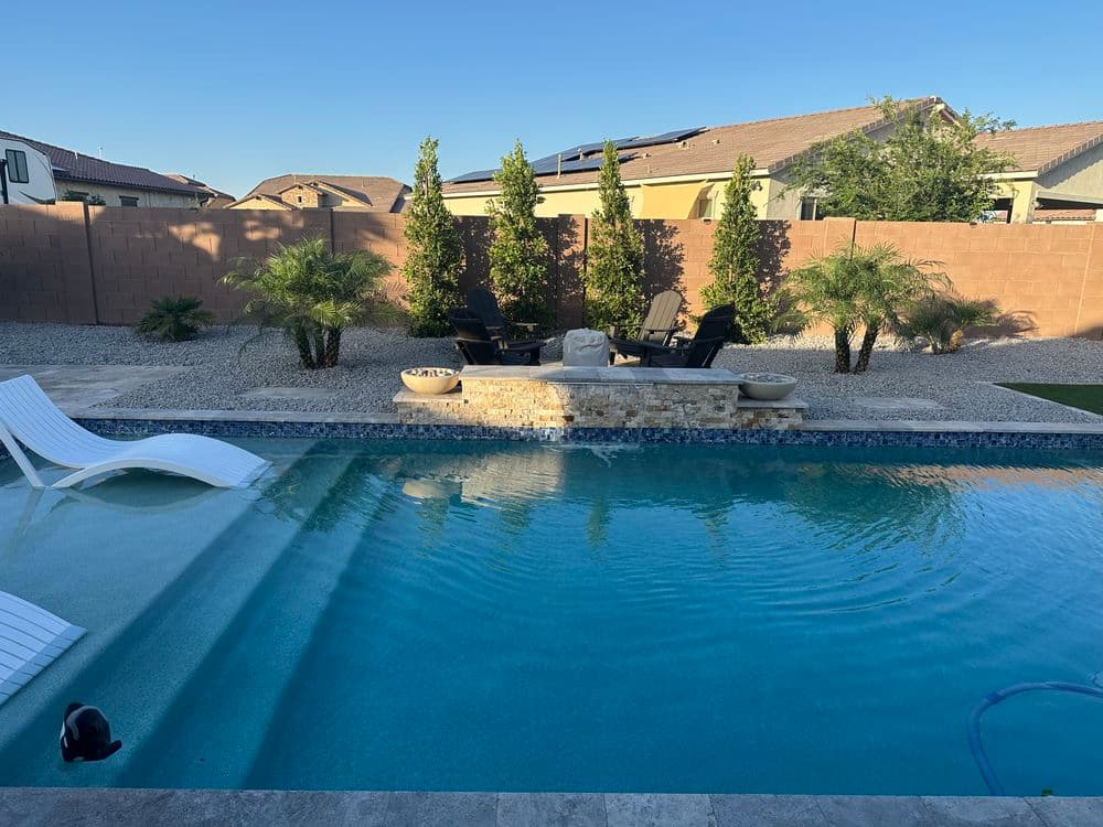 Backyard pool with lounge chairs, palm trees, and stone features in a residential setting.